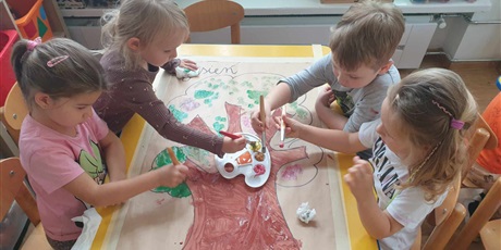 Powiększ grafikę: Dzieci siedzą przy stoliku i malują farbami drzewo