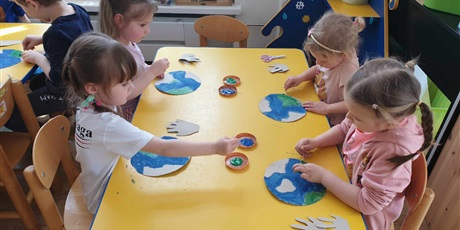 Powiększ grafikę: Przy stoliku siedzą dzieci z grupy II i malują farbami Ziemię