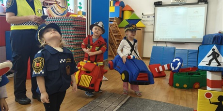 Powiększ grafikę: Dzieci w strojach policjanta, strażaka i strażnika miejskiego podczas zajęć na sali gimnastycznej "Autochodzik"