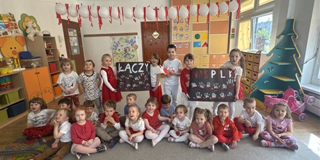 Powiększ grafikę: Na zdjęciu dzieci trzymają plakat wykonany "malowanymi farbą rączkami", na którym jest hasło: ŁĄCZY NAS POLSKA