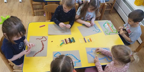 Powiększ grafikę: Dzieci z grupy II siedzą przy stoliku i wyklejają plasteliną po śladzie swoje  dinozaury