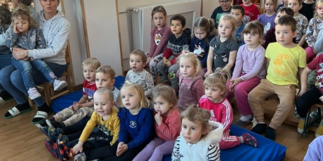 Powiększ grafikę: Dzieci z całego przedszkola podczas Koncertu na sali gimnastycznej siedzą na materacach i ławeczkach.