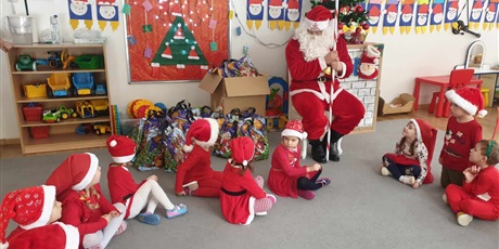 Powiększ grafikę: Św. Mikołaj siedzi na krześle, wokoło na dywanie siedzą dzieci z grupy II