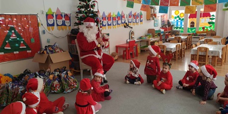 Powiększ grafikę: Św. Mikołaj siedzi na krześle, wokoło na dywanie siedzą dzieci z grupy II