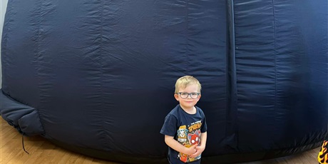 Powiększ grafikę: Na zdjęciu przedszkolak na tle kopułu Mobilnego Planetarium