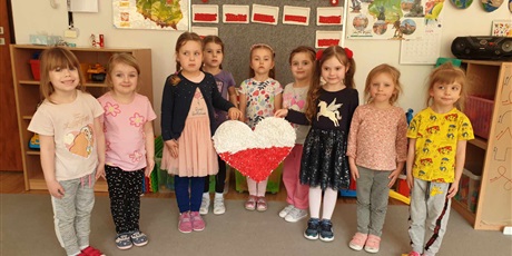 Powiększ grafikę: Na zdjęciu dziewczynki z grupy II trzymają w rękach serce biało-czerwone wykonane przez dzieci