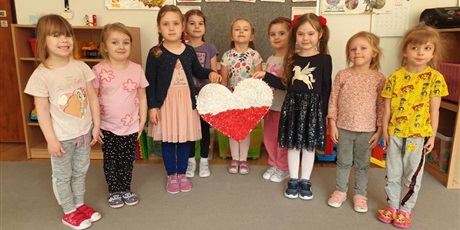 Powiększ grafikę: Na zdjęciu dziewczynki z grupy II trzymają w rękach serce biało-czerwone wykonane przez dzieci