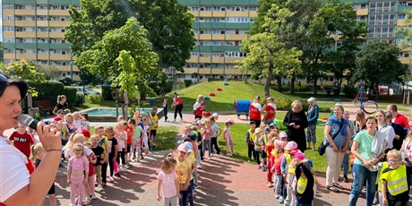 Powiększ grafikę: Dzieci z P62 w rzędach czekają na rozpoczęcie zawodów sportowych. Z lewej strony stoi Pani Iza i życzy dzieciom super zabawy.
