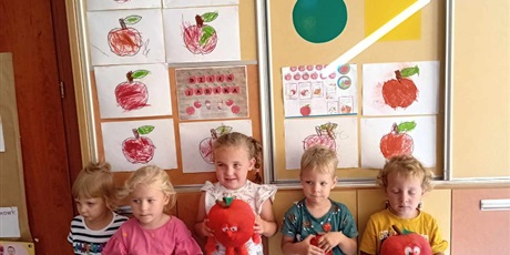 Powiększ grafikę: Grupka dzieci z grupy I trzyma w rączkach jabłuszka, na szafie wiszą prace plastyczne - oczywiście pokolorowane pięknie jabłuszka.