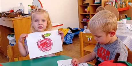 Powiększ grafikę: Przy stoliku siedzi dwoje dzieci z grupy I - dziewczynka pokazuje pięknie pokolorowane jabłuszko, chłopiec jeszcze koloruje