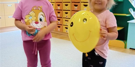 Powiększ grafikę: Dwie dziewczynki z grupy I na zdjęciu, jedna trzyma w rączkach żółtego balonika z uśmiechniętą buźką