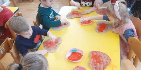 Powiększ grafikę: Dzieci siedzą przy stoliku i malują farbami czerwone serca
