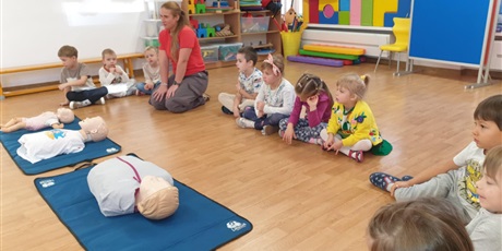 Powiększ grafikę: Zajęcia edukacyjne z udzielania pierwszej pomocy - grupa III - na zdjęciu dzieci siedzą na sali gimnastycznej na podłodze i uważnie słuchają pani instruktorki i uczą się jak przeprowadzić sztuczne oddychanie