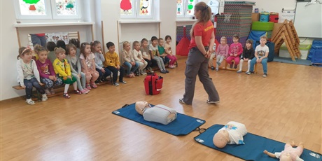 Powiększ grafikę: Zajęcia edukacyjne z udzielania pierwszej pomocy - grupa III - na zdjęciu dzieci siedzą na sali gimnastycznej na ławeczkach i uważnie słuchają pani instruktorki i uczą się jak przeprowadzić sztuczne oddychanie