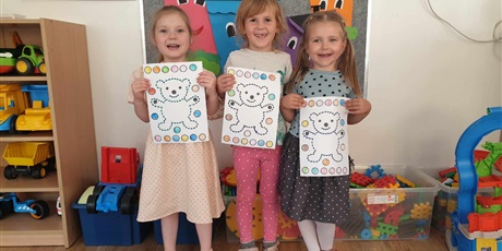 Powiększ grafikę: Na zdjęciu trzy dziewczynki z grupy II trzymają w rączkach swoje obrazki, na których jest miś i kolorowe kropki.